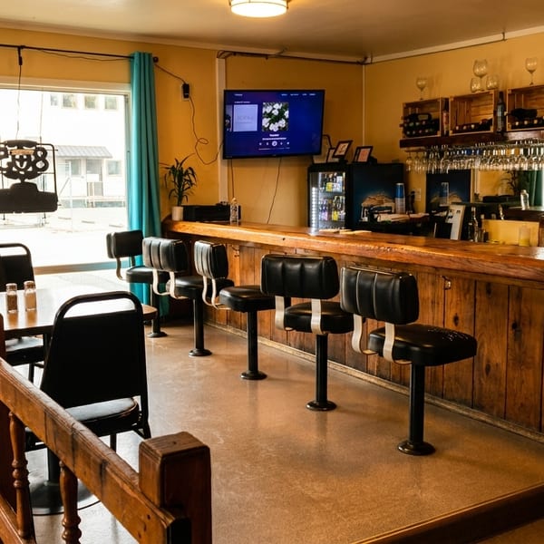 A cozy restaurant interior with a wooden bar, black stools, and dining tables near a window.